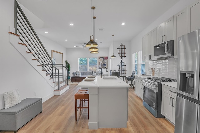 kitchen with sink, decorative backsplash, hanging light fixtures, stainless steel appliances, and a center island with sink