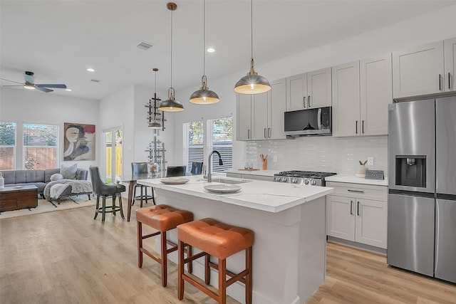 kitchen featuring sink, ceiling fan, appliances with stainless steel finishes, a center island with sink, and decorative light fixtures