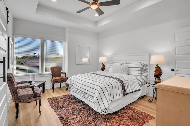 bedroom featuring a raised ceiling, ceiling fan, and light hardwood / wood-style flooring