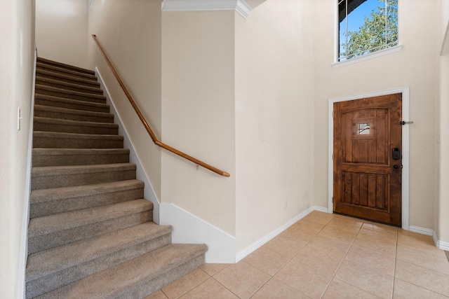 entryway with light tile patterned floors, crown molding, and a high ceiling