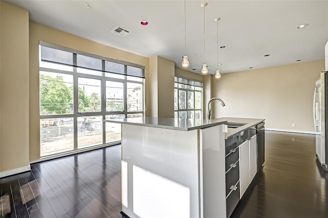 kitchen with sink, dark wood-type flooring, white cabinetry, hanging light fixtures, and a center island with sink