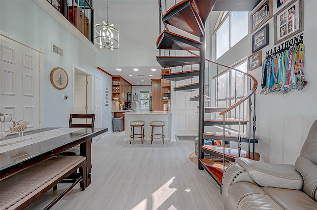 living room with a towering ceiling, sink, light hardwood / wood-style flooring, and a notable chandelier