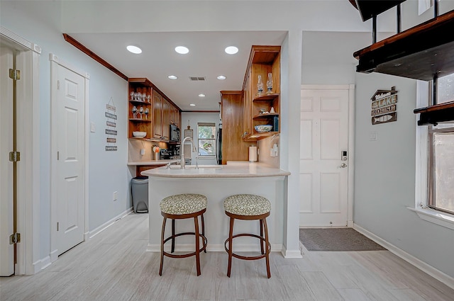 kitchen featuring ornamental molding, a kitchen bar, kitchen peninsula, and light wood-type flooring