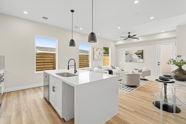 kitchen featuring decorative light fixtures, sink, white cabinets, stainless steel dishwasher, and a center island with sink