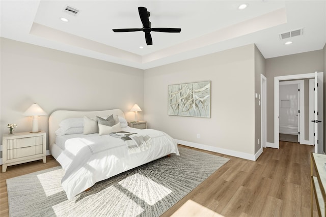 bedroom with a raised ceiling, ceiling fan, and light wood-type flooring