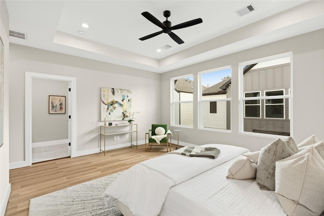 bedroom with hardwood / wood-style floors, a tray ceiling, ceiling fan, and ensuite bathroom