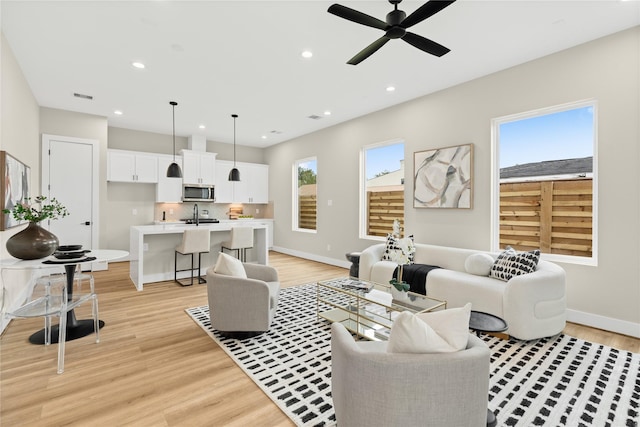 living room featuring ceiling fan, sink, and light wood-type flooring