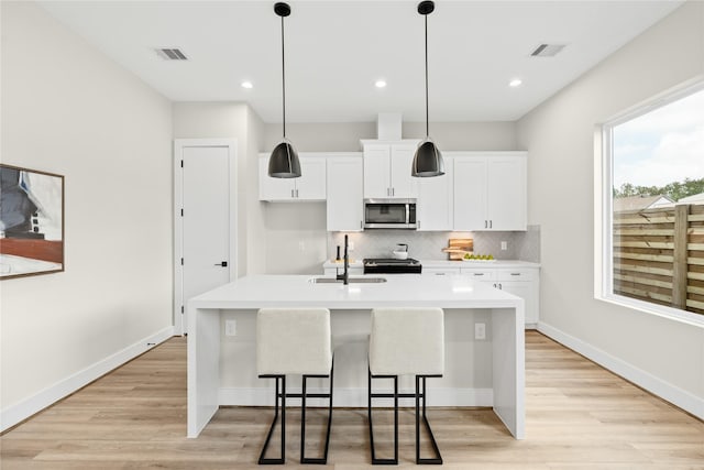 kitchen featuring decorative light fixtures, sink, a breakfast bar area, white cabinets, and a kitchen island with sink