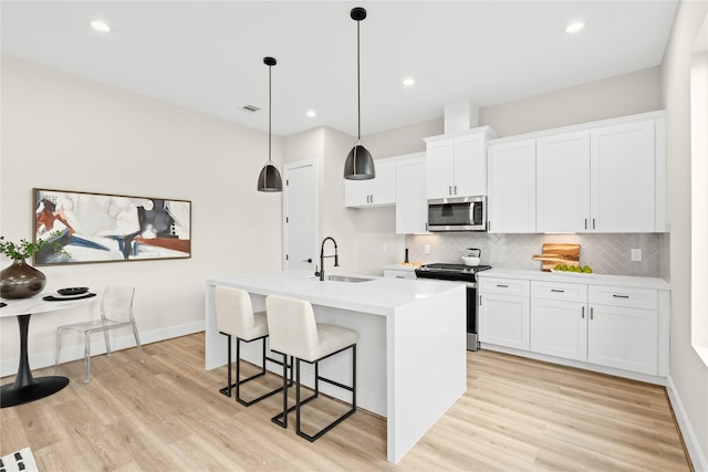 kitchen with white cabinetry, sink, stainless steel appliances, and a center island with sink