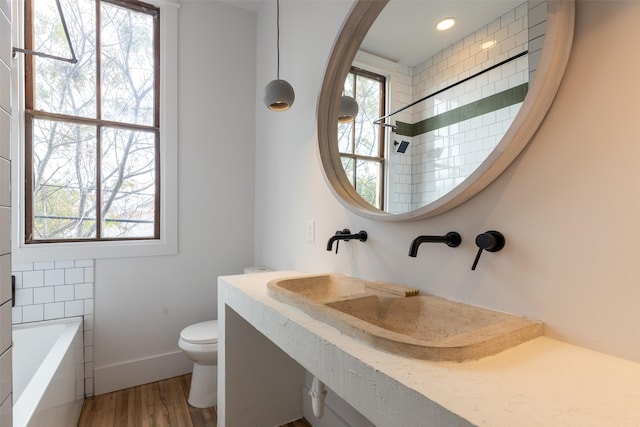 full bathroom with hardwood / wood-style floors, tiled shower / bath, sink, and toilet