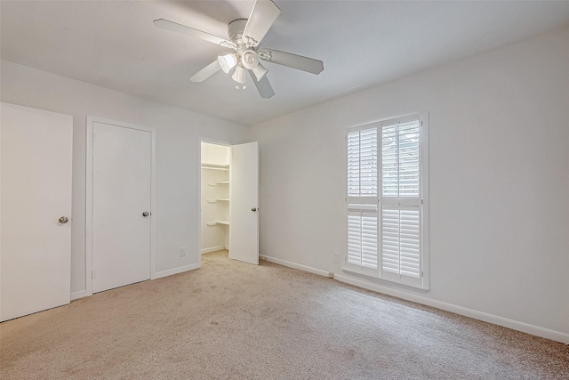 unfurnished bedroom featuring light carpet, a spacious closet, and ceiling fan