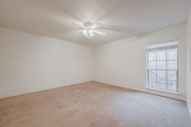 carpeted spare room featuring ceiling fan and brick wall