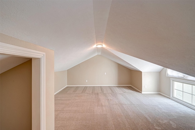 additional living space with light carpet, vaulted ceiling, and a textured ceiling