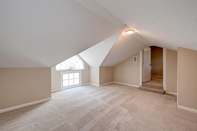 additional living space with vaulted ceiling, light carpet, and a textured ceiling