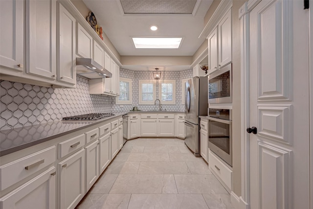 kitchen with stainless steel appliances, tasteful backsplash, white cabinets, and range hood