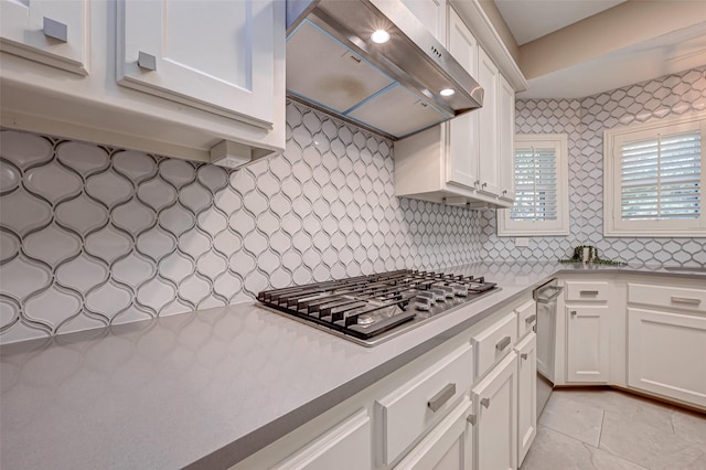 kitchen featuring exhaust hood, white cabinetry, light tile patterned floors, stainless steel gas stovetop, and backsplash