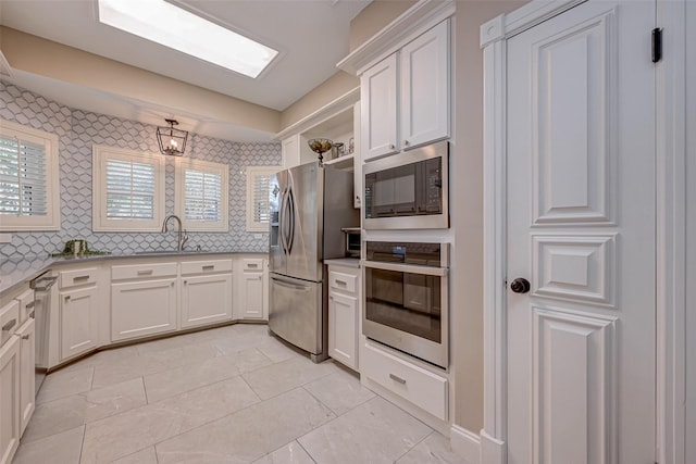 kitchen featuring sink, white cabinets, decorative backsplash, light tile patterned floors, and stainless steel appliances