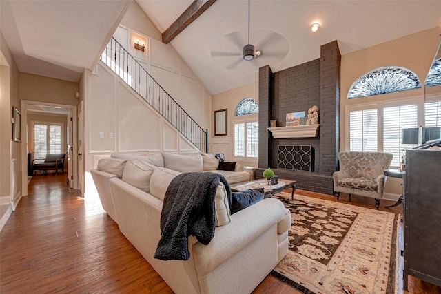 living room featuring a fireplace, high vaulted ceiling, ceiling fan, beam ceiling, and hardwood / wood-style floors