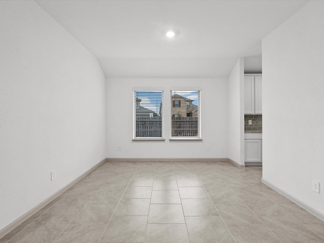 tiled empty room featuring lofted ceiling