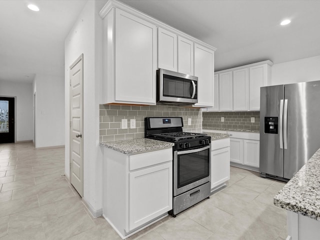 kitchen with light tile patterned flooring, appliances with stainless steel finishes, light stone countertops, decorative backsplash, and white cabinets