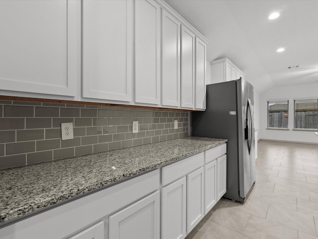 kitchen featuring white cabinetry, light tile patterned floors, stainless steel fridge, light stone countertops, and decorative backsplash