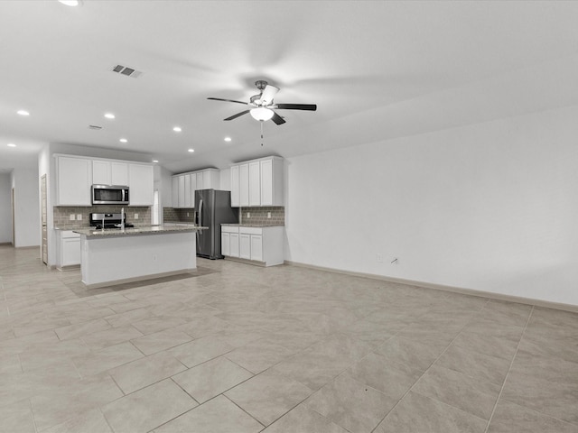 kitchen with stainless steel appliances, a kitchen island with sink, white cabinets, and light stone counters