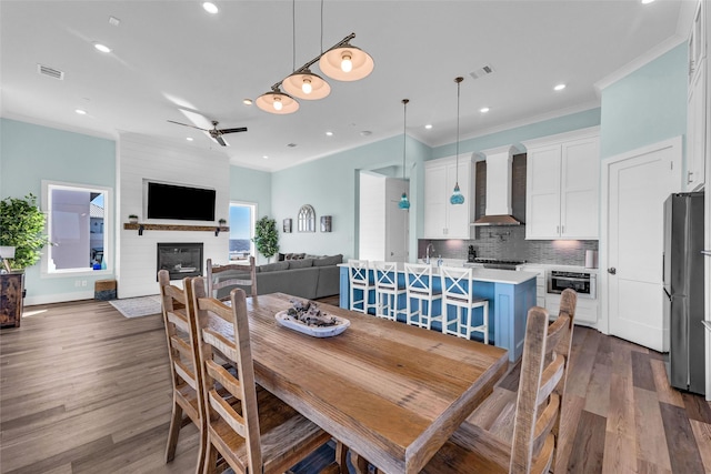 dining area with ceiling fan, crown molding, a fireplace, and dark wood-type flooring