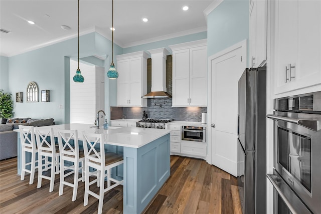 kitchen with wall chimney range hood, white cabinetry, appliances with stainless steel finishes, and a breakfast bar area