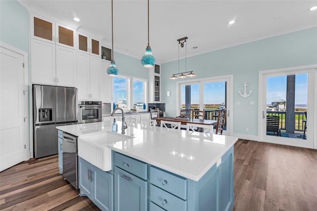 kitchen featuring pendant lighting, an island with sink, sink, white cabinets, and stainless steel appliances