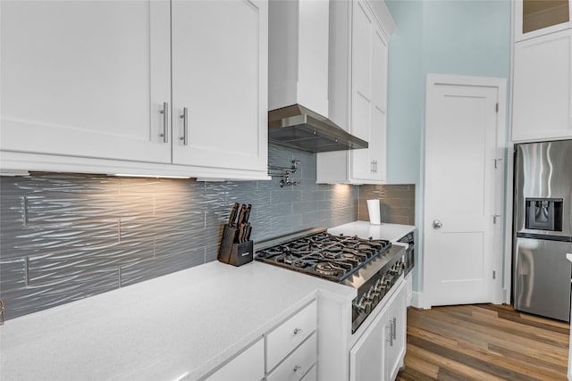 kitchen with appliances with stainless steel finishes, white cabinets, backsplash, dark wood-type flooring, and wall chimney range hood