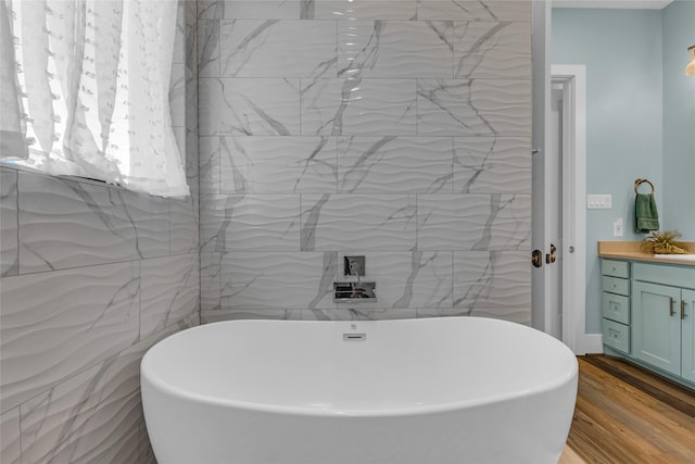 bathroom featuring hardwood / wood-style flooring, a tub to relax in, vanity, and tile walls