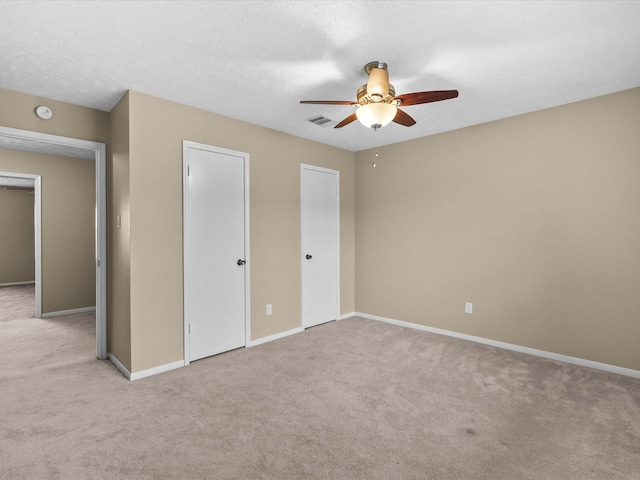 unfurnished bedroom featuring two closets, light colored carpet, ceiling fan, and a textured ceiling