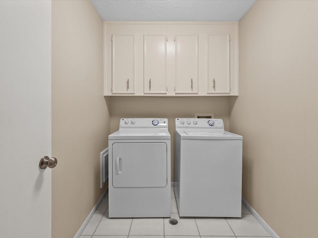 laundry area featuring light tile patterned flooring, cabinets, washing machine and dryer, and a textured ceiling