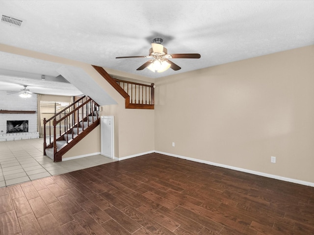 unfurnished living room featuring a brick fireplace, a textured ceiling, and ceiling fan