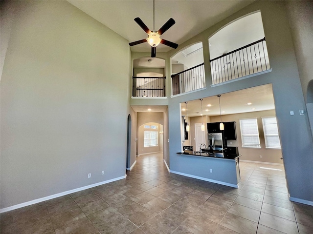 unfurnished living room featuring ceiling fan, a towering ceiling, plenty of natural light, and dark tile patterned floors