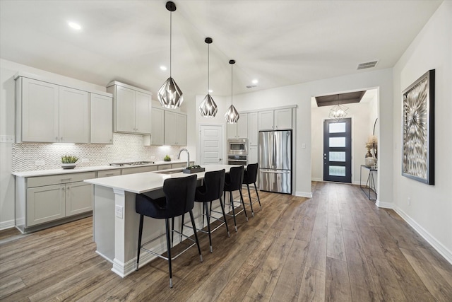 kitchen with sink, a breakfast bar, appliances with stainless steel finishes, a kitchen island with sink, and dark hardwood / wood-style flooring