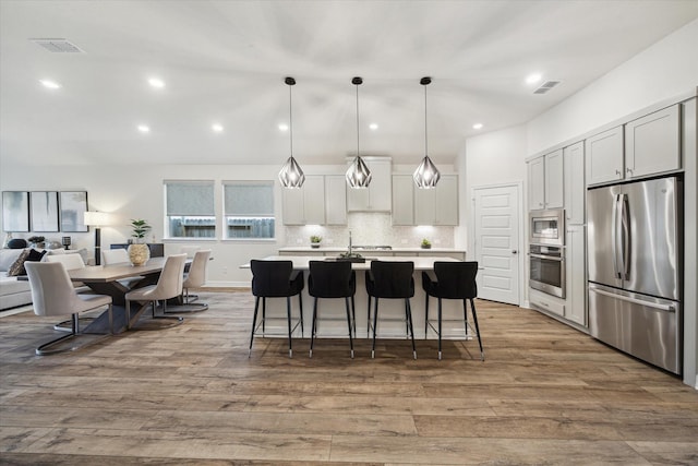 kitchen with appliances with stainless steel finishes, pendant lighting, white cabinetry, wood-type flooring, and a center island with sink