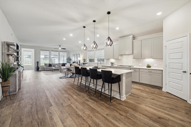 kitchen featuring a breakfast bar, sink, decorative light fixtures, hardwood / wood-style flooring, and a kitchen island with sink