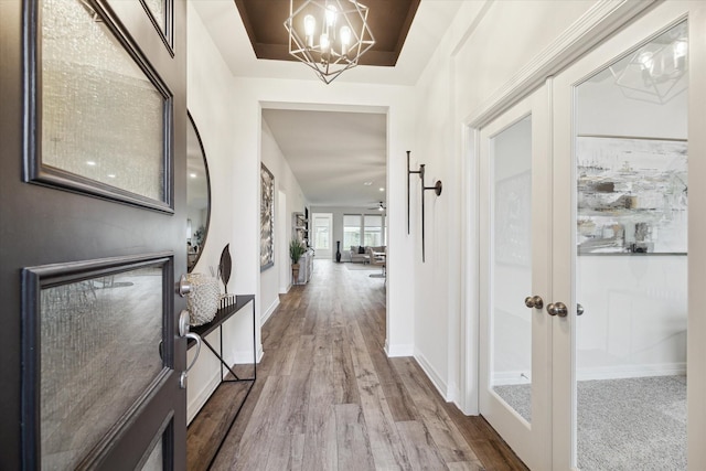 foyer entrance featuring an inviting chandelier, a tray ceiling, wood-type flooring, and french doors