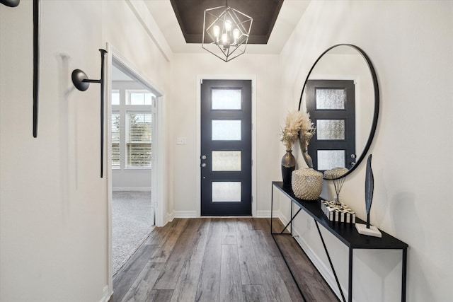 foyer entrance with a notable chandelier, wood-type flooring, and a raised ceiling