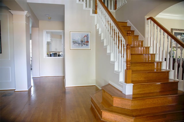 stairs featuring decorative columns, crown molding, and wood-type flooring