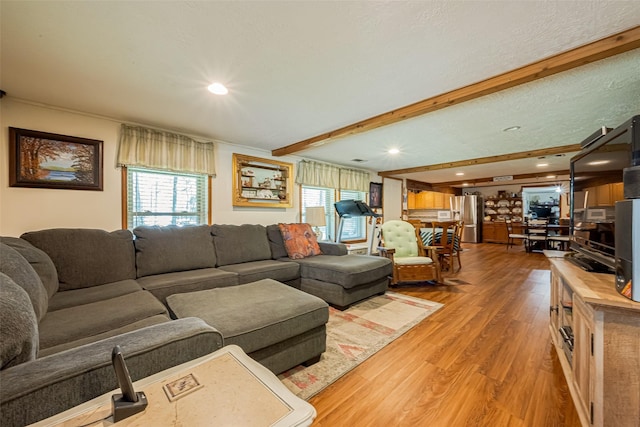 living area with beam ceiling, a healthy amount of sunlight, a textured ceiling, and wood finished floors