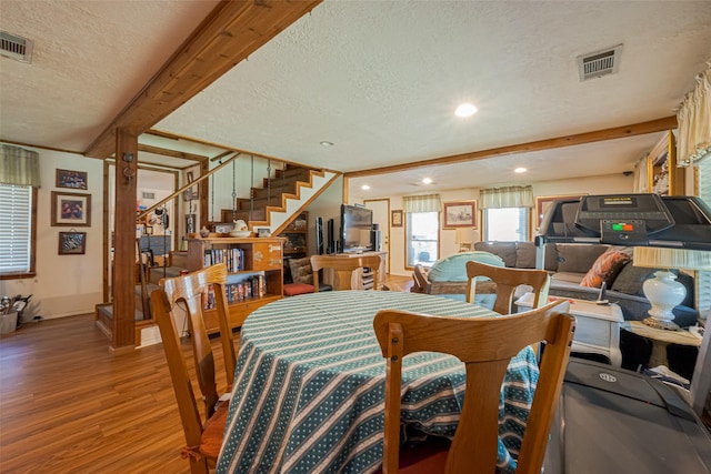 dining space with visible vents, stairway, beamed ceiling, wood finished floors, and a textured ceiling