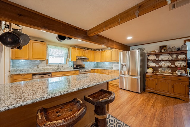 kitchen with stainless steel appliances, light wood-style floors, light stone countertops, beamed ceiling, and under cabinet range hood