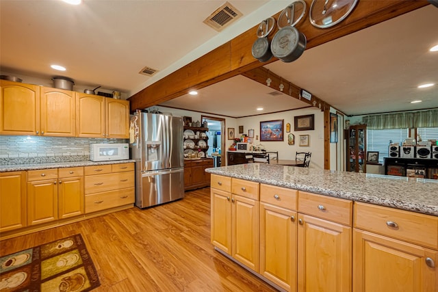 kitchen featuring visible vents, stainless steel fridge with ice dispenser, white microwave, light stone counters, and beamed ceiling