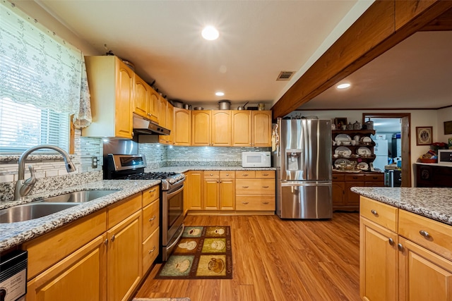 kitchen with under cabinet range hood, stainless steel appliances, a sink, light wood-type flooring, and light stone countertops