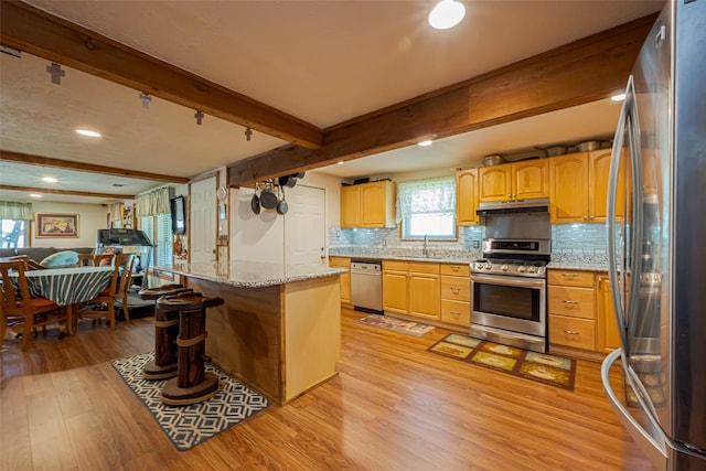 kitchen featuring light wood-style floors, appliances with stainless steel finishes, open floor plan, under cabinet range hood, and a sink