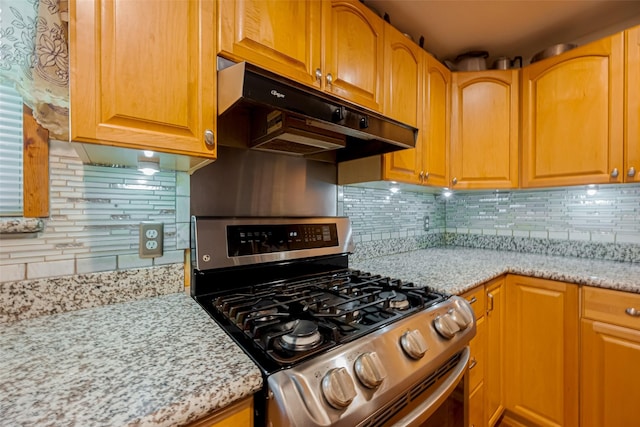 kitchen with stainless steel gas stove, under cabinet range hood, backsplash, and light stone countertops