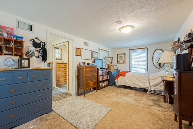 bedroom featuring visible vents, a textured ceiling, and light colored carpet