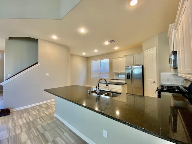 kitchen featuring sink, white cabinetry, appliances with stainless steel finishes, kitchen peninsula, and dark stone counters